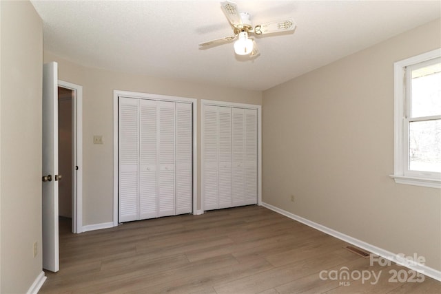 unfurnished bedroom with baseboards, two closets, visible vents, and light wood-style floors