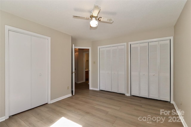 unfurnished bedroom featuring a ceiling fan, two closets, light wood-style flooring, and baseboards