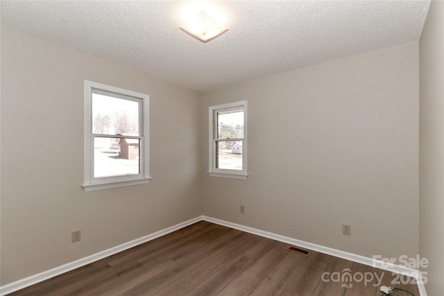 spare room featuring dark wood-style flooring, visible vents, a textured ceiling, and baseboards