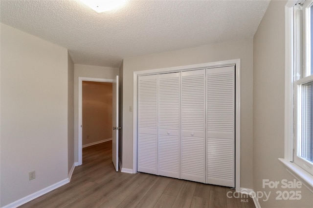 unfurnished bedroom featuring light wood-type flooring, a closet, a textured ceiling, and baseboards