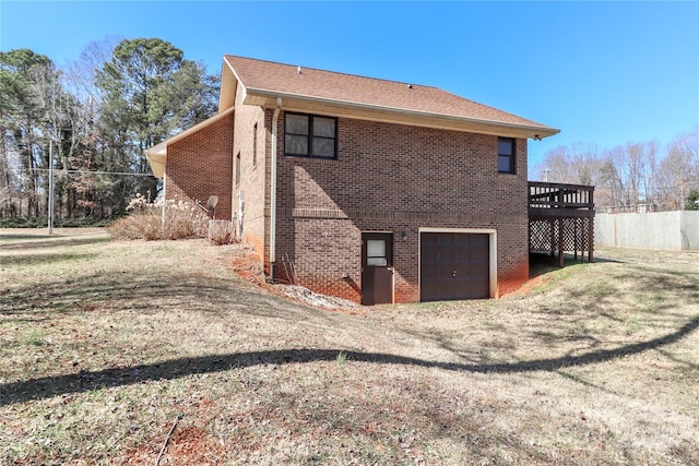 rear view of property featuring a garage, driveway, brick siding, and a wooden deck