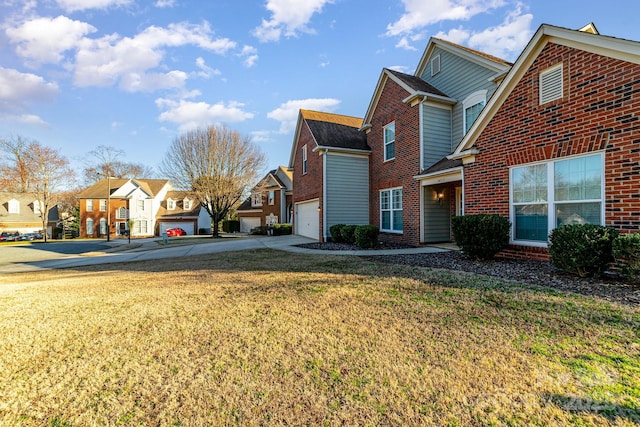 view of side of home featuring a garage, brick siding, driveway, a lawn, and a residential view