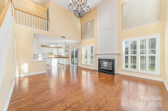 unfurnished living room featuring light wood-style floors, baseboards, an inviting chandelier, and a high end fireplace