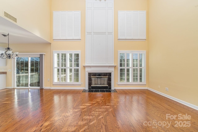 unfurnished living room with a notable chandelier, a fireplace, a high ceiling, wood finished floors, and baseboards