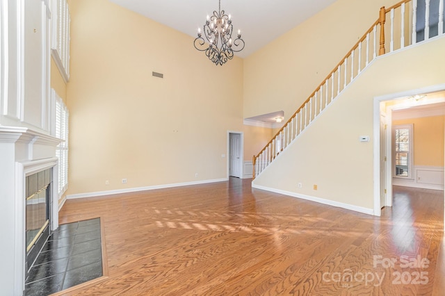 unfurnished living room with a wealth of natural light, stairs, wood finished floors, and a tile fireplace