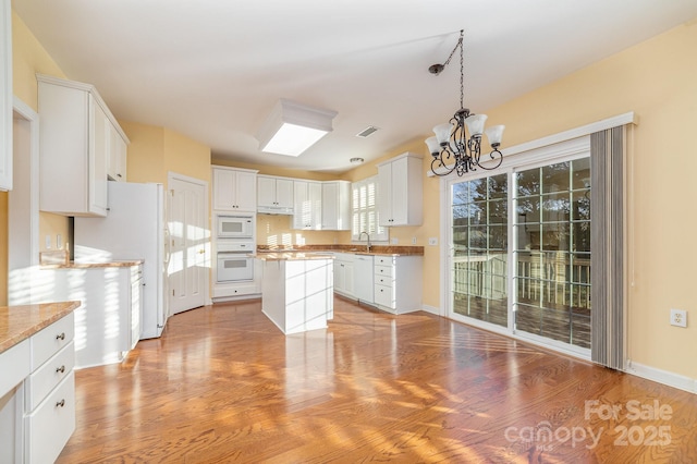 kitchen with light wood-style flooring, white appliances, a sink, white cabinetry, and an inviting chandelier