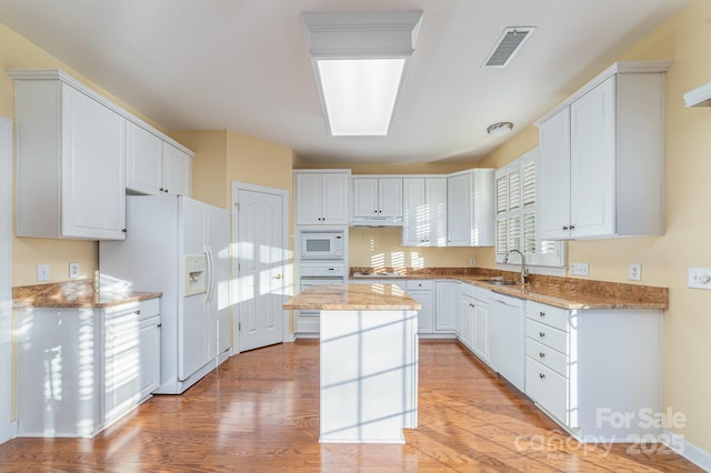 kitchen featuring visible vents, white cabinets, a kitchen island, a sink, and white appliances