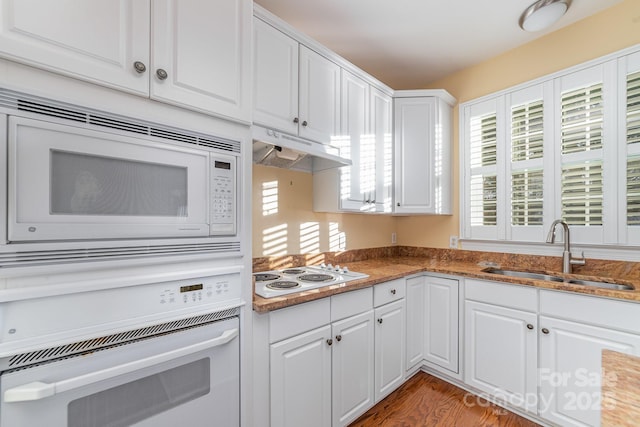 kitchen with under cabinet range hood, white appliances, a sink, white cabinetry, and dark stone counters