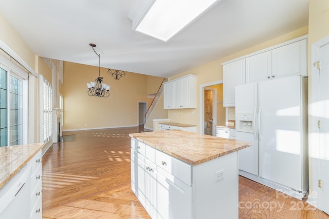 kitchen with white refrigerator with ice dispenser, white cabinetry, a kitchen island, and decorative light fixtures