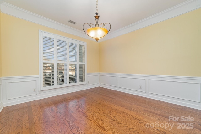 spare room featuring a chandelier, wood finished floors, visible vents, ornamental molding, and wainscoting