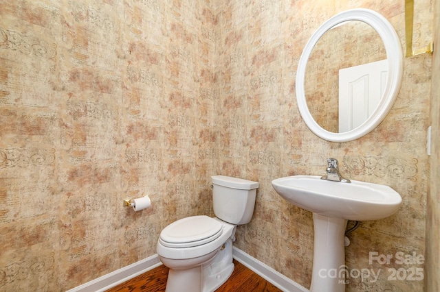 half bathroom featuring baseboards, toilet, and wood finished floors