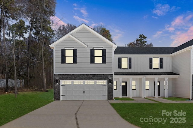 view of front of home with a garage, concrete driveway, stone siding, a front lawn, and board and batten siding