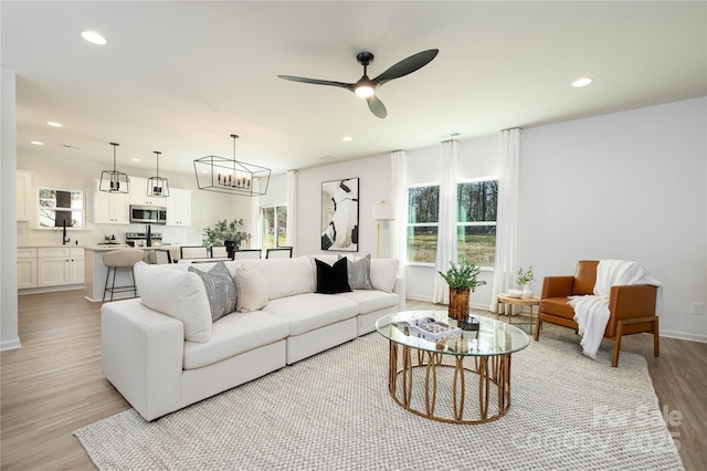 living area with light wood-style flooring, ceiling fan with notable chandelier, and recessed lighting