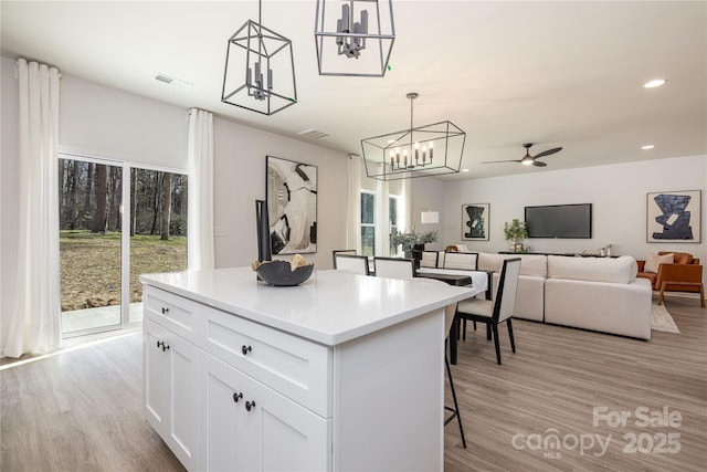 kitchen with visible vents, a kitchen island, light wood-style flooring, and white cabinetry