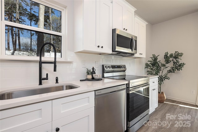 kitchen with stainless steel appliances, a sink, white cabinetry, light countertops, and backsplash