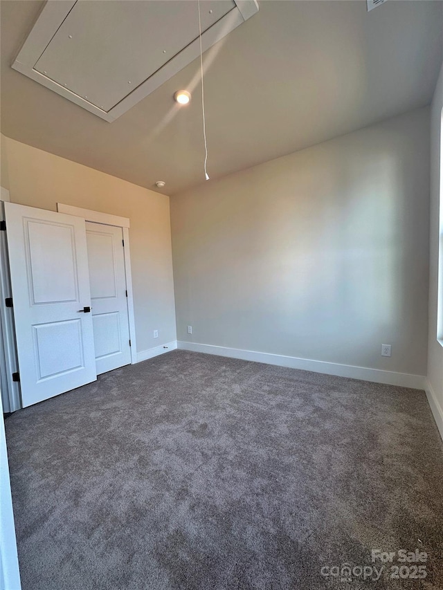 empty room with dark carpet, attic access, and baseboards