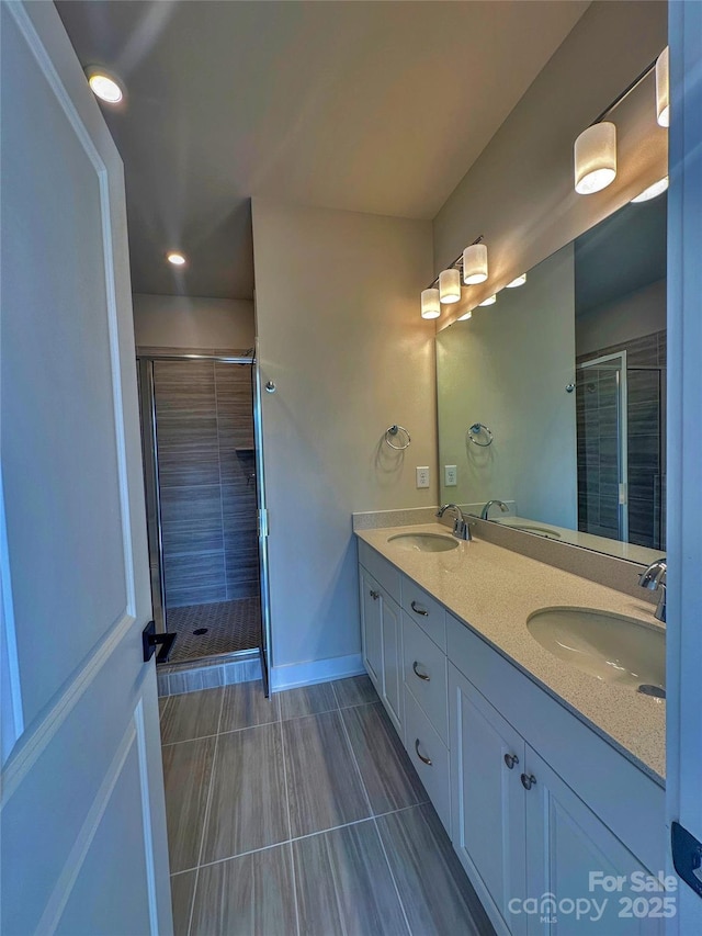 full bathroom with double vanity, a stall shower, a sink, and baseboards