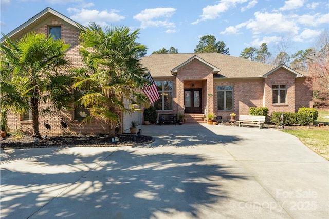 view of front of home featuring a shingled roof, brick siding, and driveway