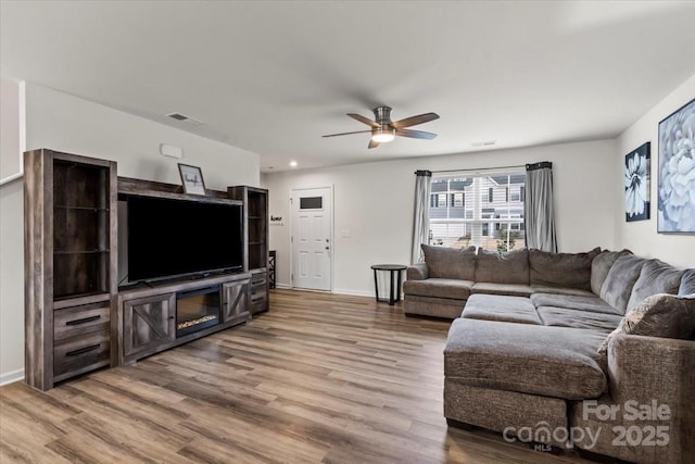 living area featuring a ceiling fan, baseboards, visible vents, and wood finished floors