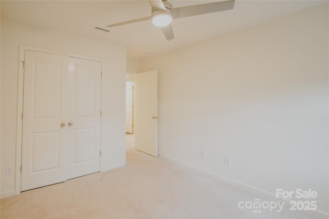 unfurnished bedroom with a ceiling fan, a closet, light colored carpet, and baseboards