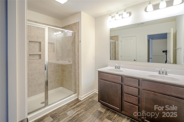 bathroom featuring double vanity, wood finished floors, a stall shower, and a sink