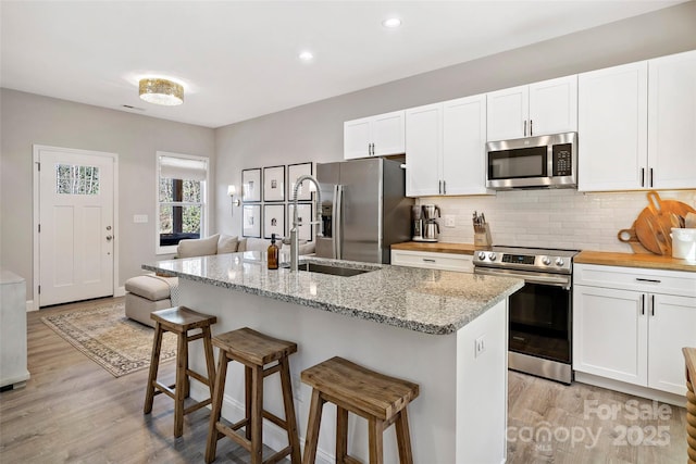 215 David Ridge Rd, Black Mountain, NC 28711 - kitchen featuring a breakfast bar area, stainless steel appliances, tasteful backsplash, a kitchen island with sink, and white cabinetry