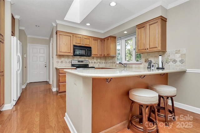 kitchen with black microwave, a peninsula, stainless steel range with electric cooktop, white fridge with ice dispenser, and light wood finished floors