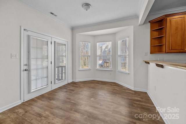 unfurnished dining area featuring baseboards, visible vents, ornamental molding, and wood finished floors