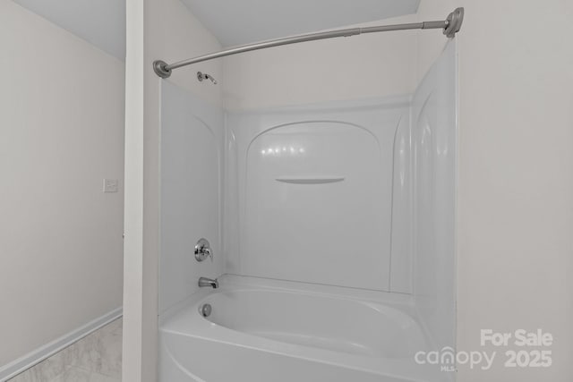 bathroom featuring washtub / shower combination, marble finish floor, and baseboards