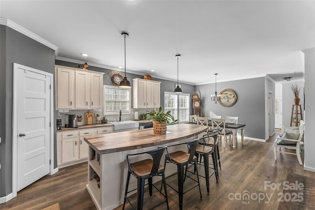 kitchen with pendant lighting, dark wood-style flooring, a sink, a kitchen island, and butcher block countertops