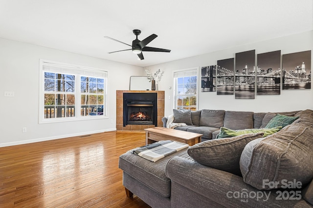 living area featuring visible vents, a tiled fireplace, ceiling fan, wood finished floors, and baseboards