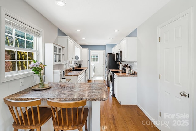 kitchen with appliances with stainless steel finishes, glass insert cabinets, white cabinets, a peninsula, and a kitchen bar