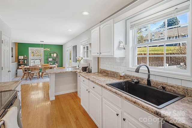 kitchen with a sink, white cabinetry, hanging light fixtures, light wood-type flooring, and tasteful backsplash