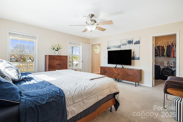 bedroom with a walk in closet, a closet, a ceiling fan, light carpet, and baseboards