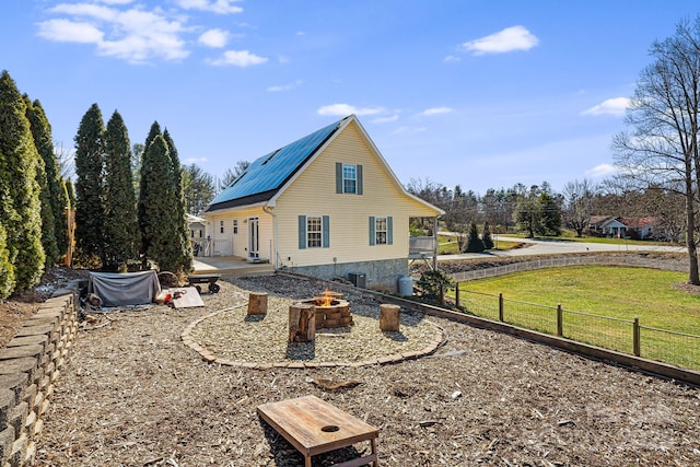 rear view of property with an outdoor fire pit, fence, metal roof, and a lawn