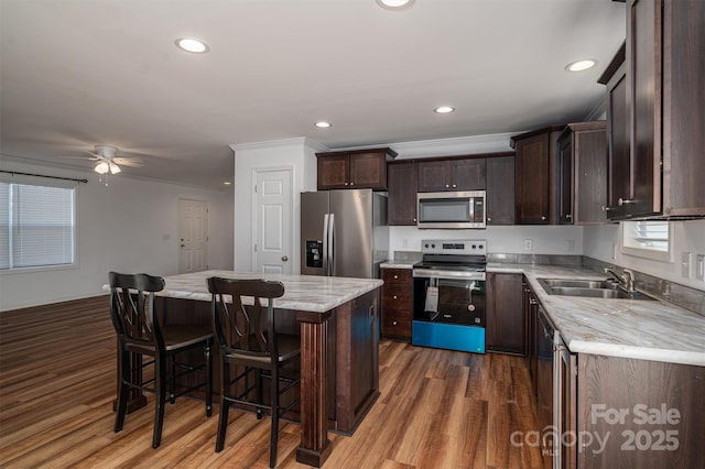 kitchen featuring stainless steel appliances, a sink, a kitchen breakfast bar, light countertops, and a center island