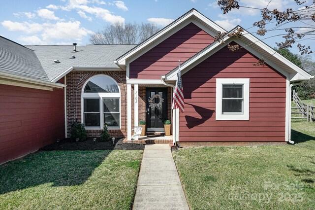 ranch-style house featuring a front lawn, roof with shingles, and brick siding