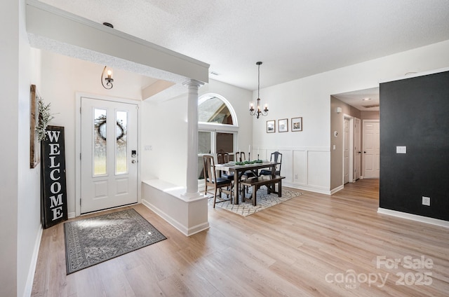 entryway with a textured ceiling, light wood-type flooring, ornate columns, a decorative wall, and a notable chandelier