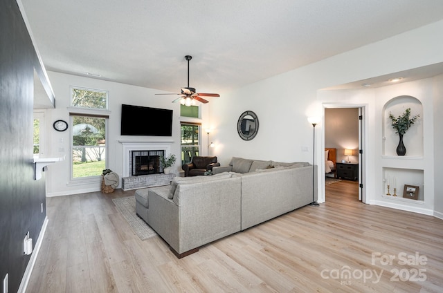 living room with light wood-type flooring, a fireplace with raised hearth, ceiling fan, and baseboards