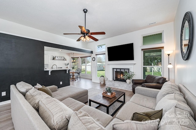 living room featuring a fireplace, light wood finished floors, visible vents, ceiling fan, and baseboards