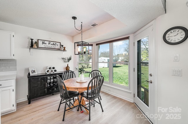 dining area with visible vents, a healthy amount of sunlight, light wood-style flooring, and a textured ceiling