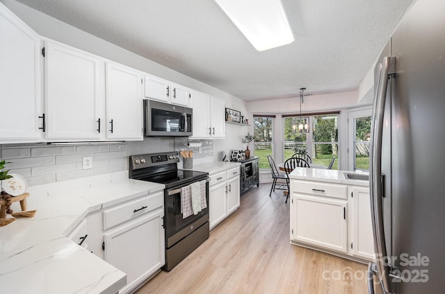 kitchen with stainless steel appliances, white cabinetry, and light wood finished floors