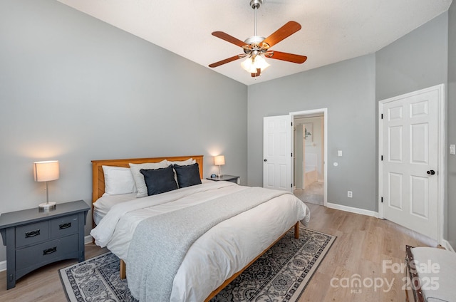 bedroom featuring light wood finished floors, ensuite bath, baseboards, and vaulted ceiling