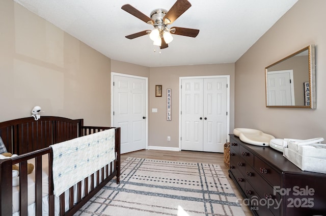 bedroom featuring light wood finished floors, a closet, ceiling fan, a nursery area, and baseboards