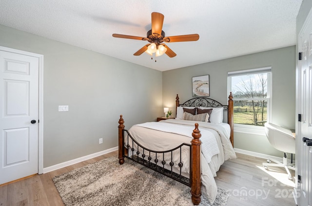 bedroom featuring ceiling fan, a textured ceiling, light wood-style flooring, and baseboards