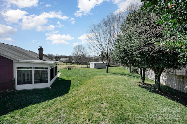 view of yard featuring a sunroom, a fenced backyard, a storage unit, and an outbuilding