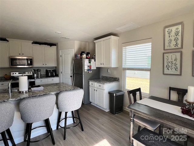 kitchen featuring appliances with stainless steel finishes, light wood-type flooring, stone counters, a kitchen bar, and white cabinetry