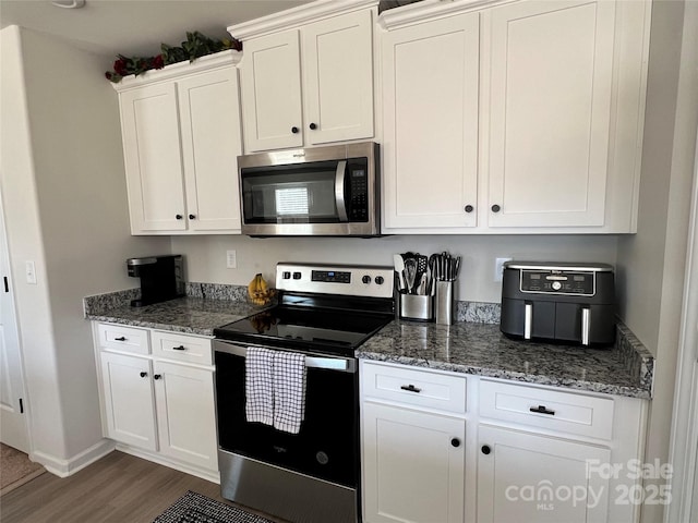 kitchen with baseboards, dark stone countertops, dark wood-type flooring, stainless steel appliances, and white cabinetry