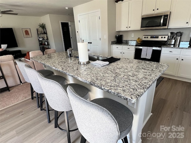 kitchen featuring appliances with stainless steel finishes, light stone counters, an island with sink, and a kitchen bar