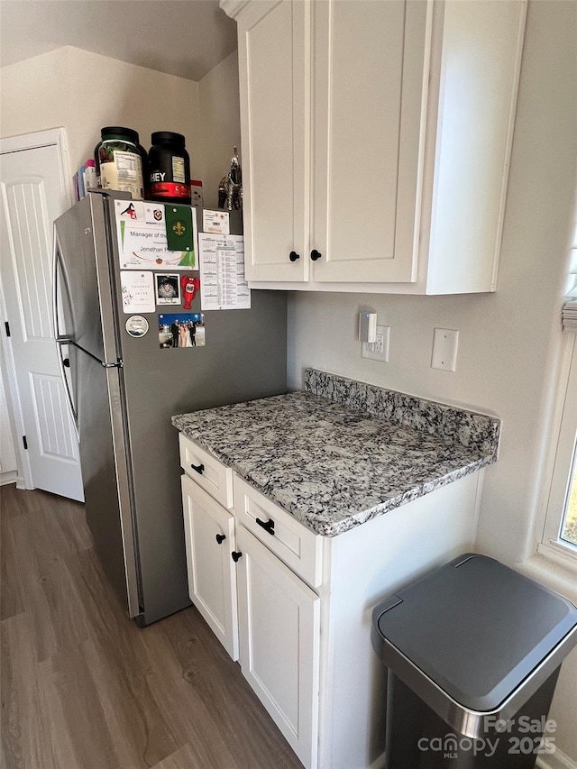 kitchen with light stone countertops, white cabinets, dark wood-style flooring, and freestanding refrigerator